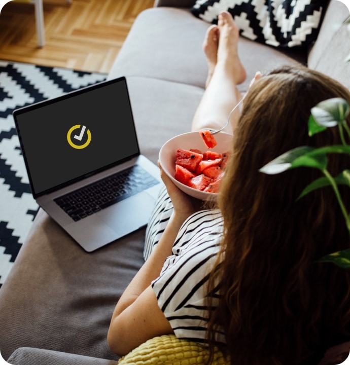 rapariga a comer melancia no sofá com um portátil a iniciar o Norton 360 Antivirus Plus.